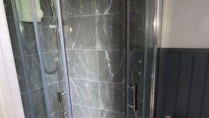 A glass-enclosed shower with a marble tile interior, a white towel on the floor, and a toilet paper holder on the wall. - The Hall Park Hotel (Workington)