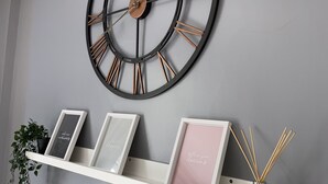 A wall-mounted clock with Roman numerals and a shelf below it holding framed pictures and a reed diffuser. - The Hall Park Hotel (Workington)