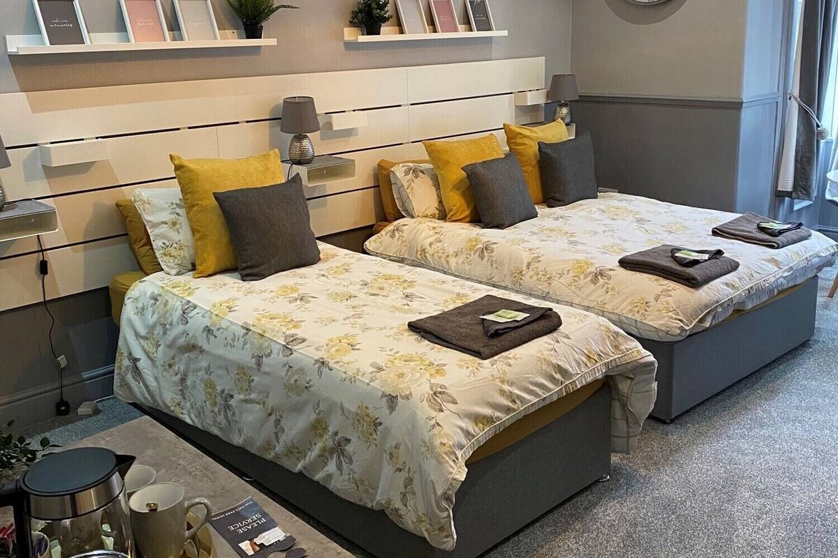 A modern hotel room with two beds, a coffee table, a clock, and a shelf with framed photos.