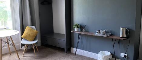 Una habitación de hotel moderna con cama, escritorio, televisor y una pequeña mesa con una planta y un hervidor.