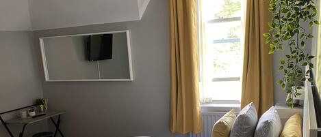 A hotel room with two beds, a desk, a TV, and a window with curtains.