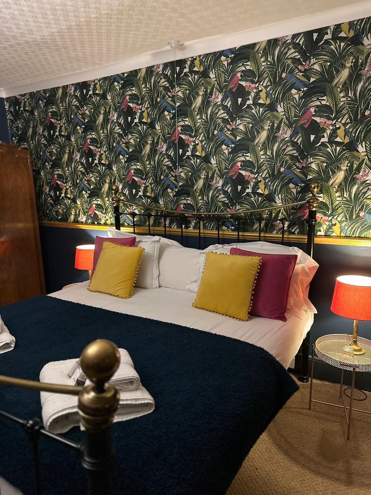 A hotel room with a bed, a nightstand, a lamp, and a wall with a tropical wallpaper.