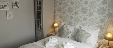 A neatly made bed with white linens and pillows, a bedside table with a lamp, and floral wallpaper.