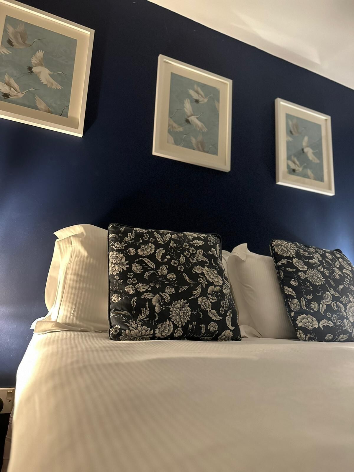 Ein Bett mit weißer Bettwäsche und Kissen mit Blumenmuster vor einer dunkelblauen Wand.