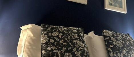 Ein Bett mit weißer Bettwäsche und Kissen mit Blumenmuster vor einer dunkelblauen Wand.