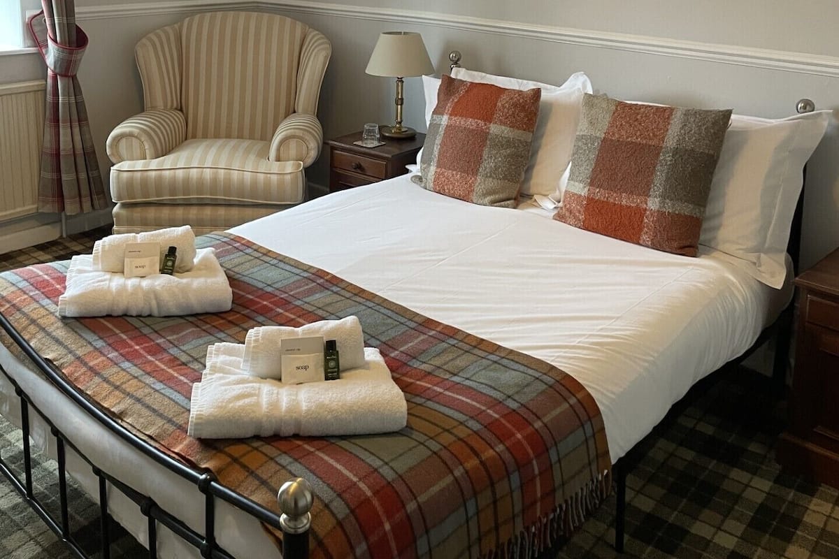 A hotel room with a bed, a chair, a nightstand, a lamp, and a window with curtains.
