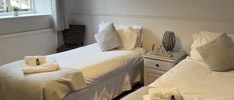Habitación de hotel con dos camas, una ventana con cortinas, una mesita de noche con lámpara y un radiador.