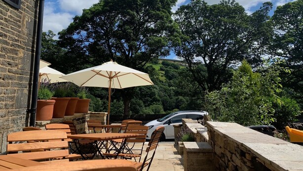 Een terras met houten tafels en stoelen, beige parasols en potplanten.