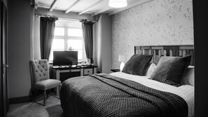 Een hotelkamer met een bed, een bureau met een televisie, een stoel en een raam met gordijnen.