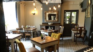 Een restaurant met houten tafels en stoelen, een geruit vloertje en hangende lampen.