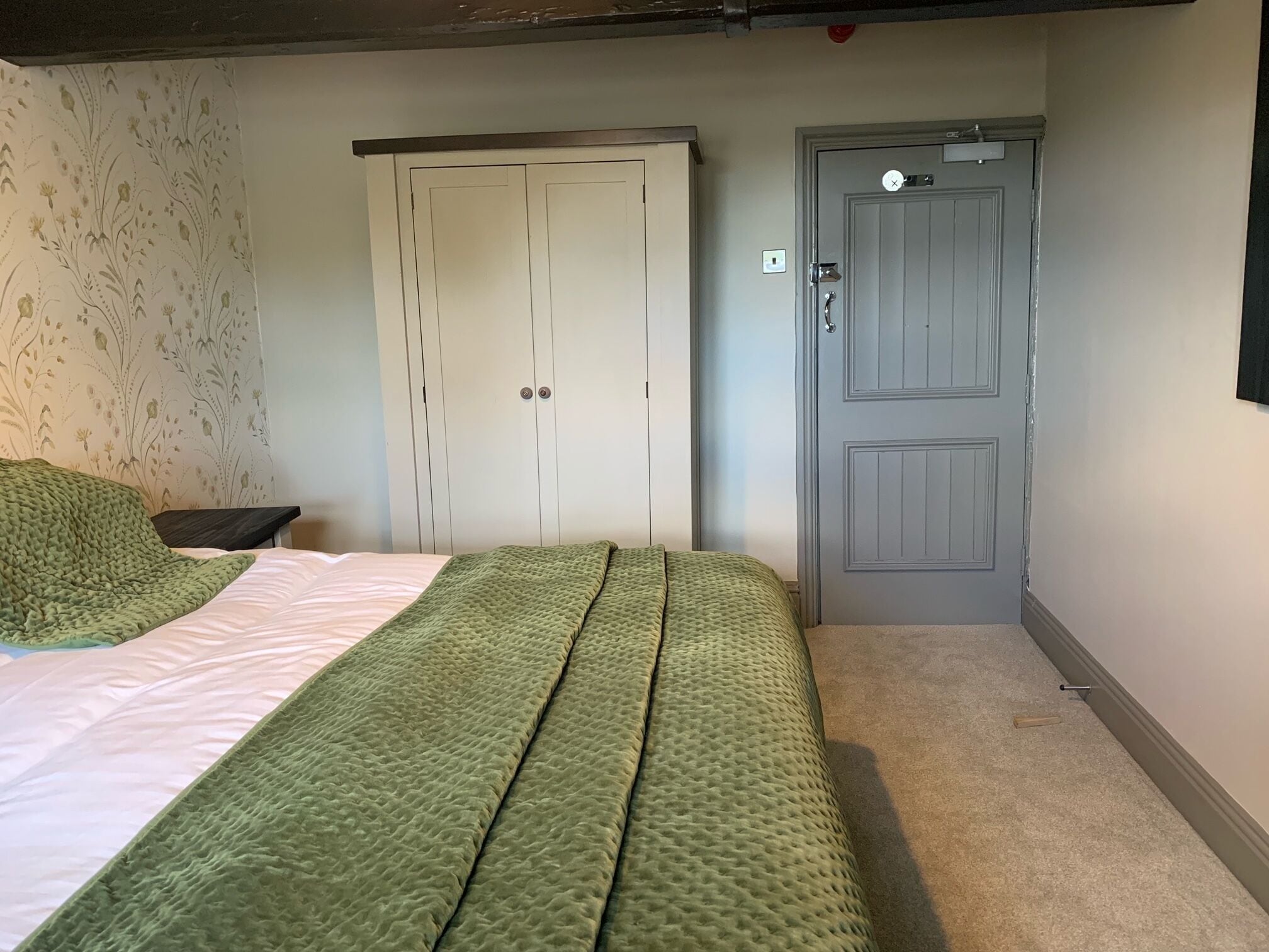 A bedroom with a bed, a green quilt, a wardrobe, and a door.