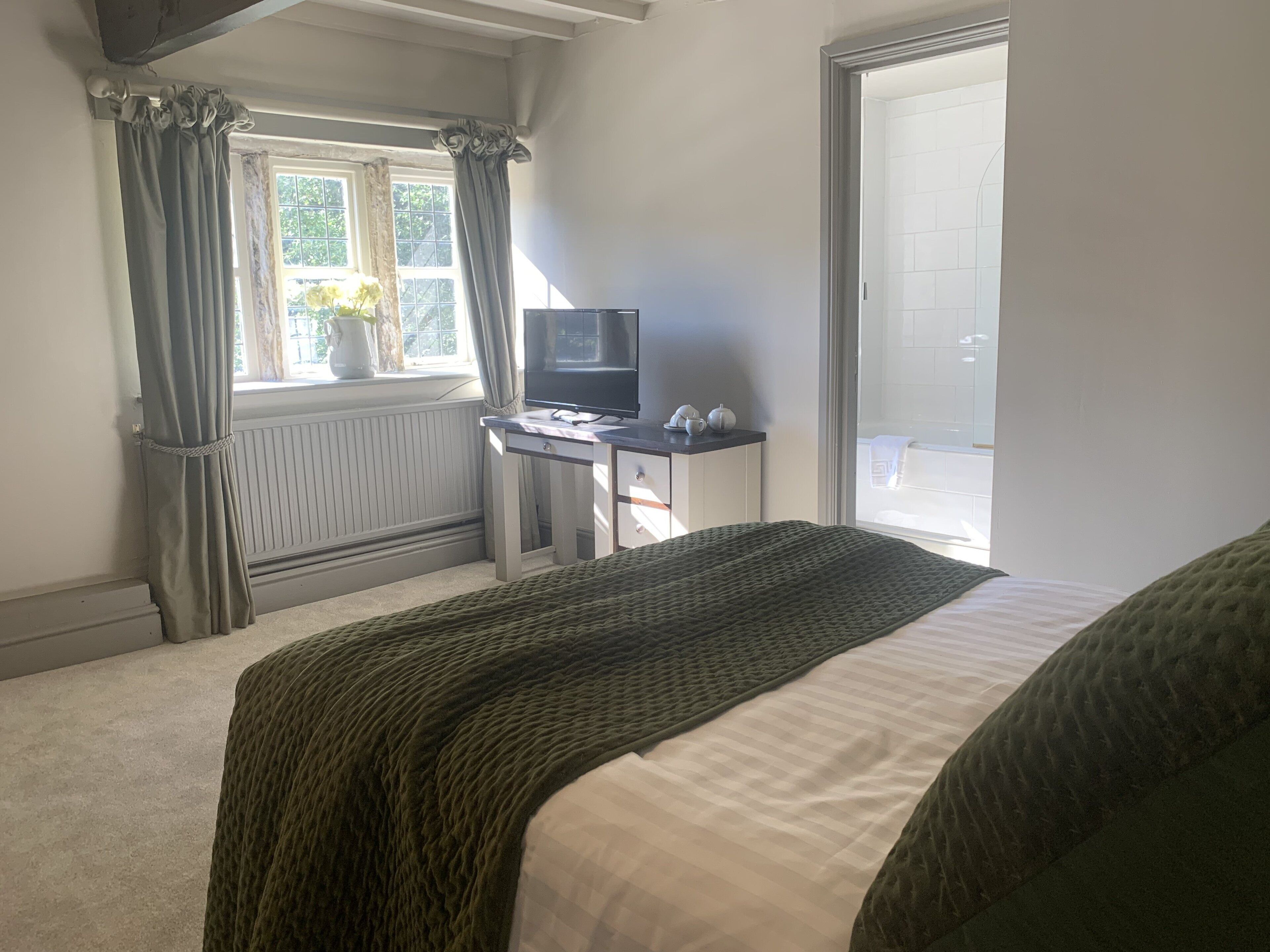 A bedroom with a bed, a desk with a computer, a window with curtains, and a radiator.
