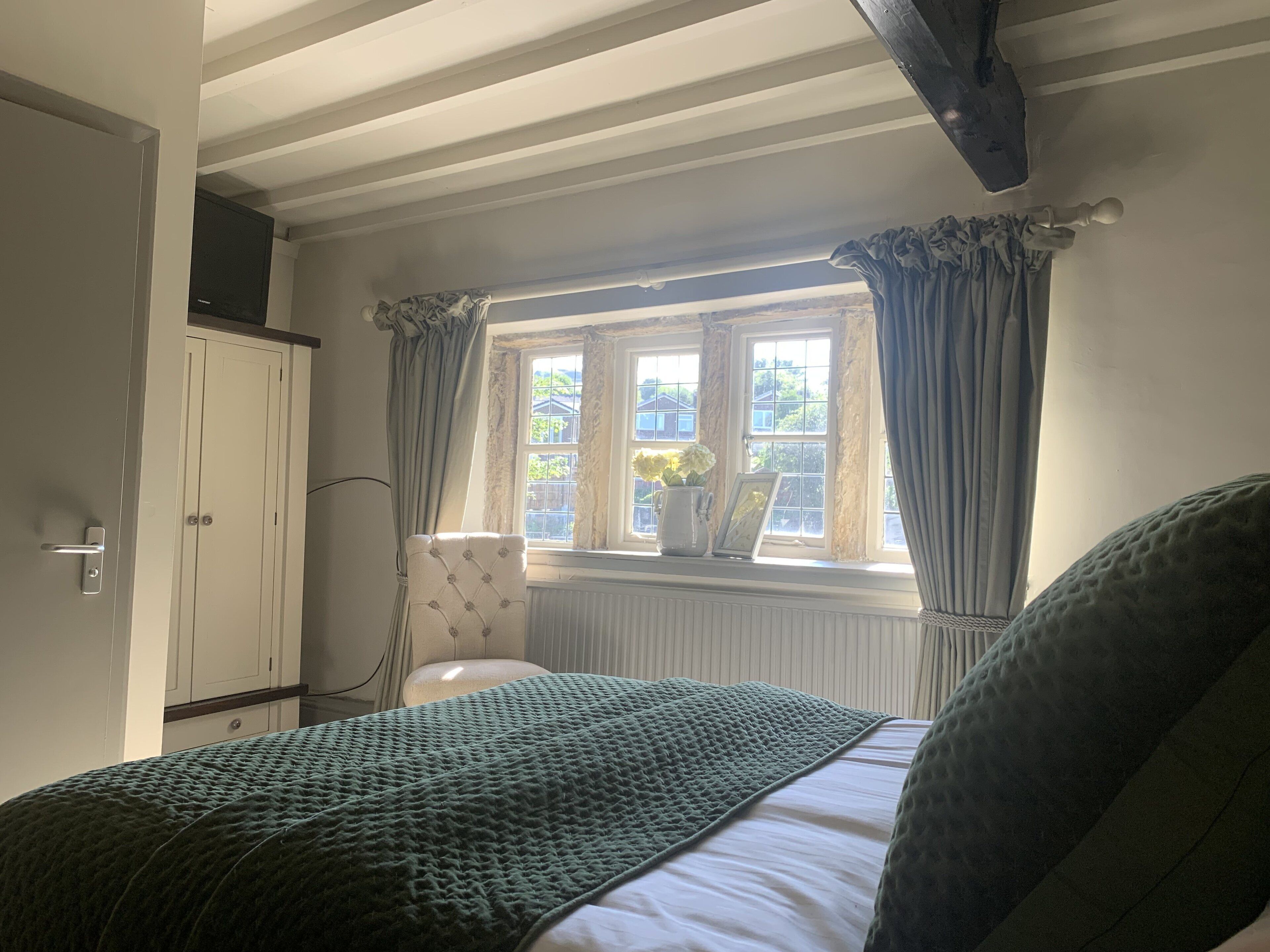 A bedroom with a bed, a chair, a window with curtains, and a radiator.