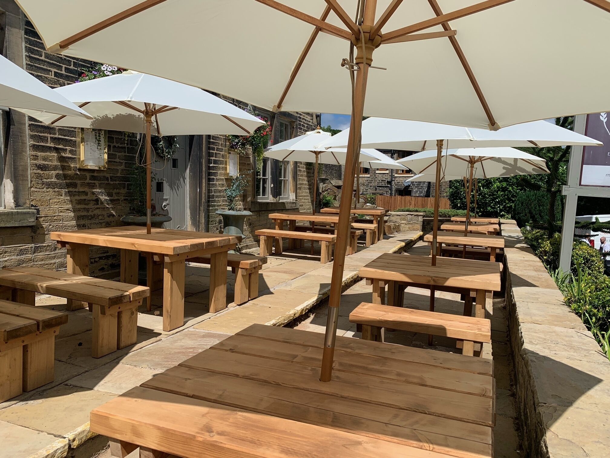Une terrasse extérieure avec des tables et des bancs en bois, protégée par des parasols blancs.