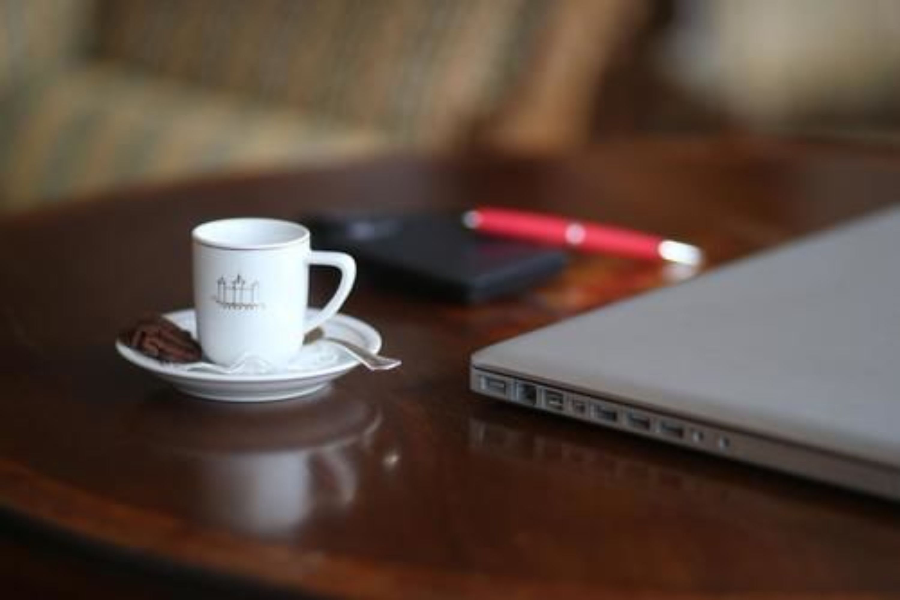 Ein Laptop auf einem Holztisch, neben ihm eine weiße Tasse und ein roter Stift.