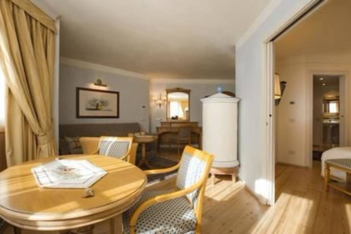 Habitación de hotel con una cama, una mesa de comedor con sillas, un armario blanco y un cuadro en la pared.