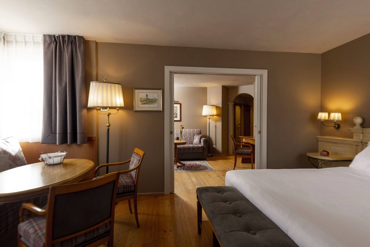 Una habitación de hotel con cama, escritorio, dos sillas, lámpara y una pequeña mesa.