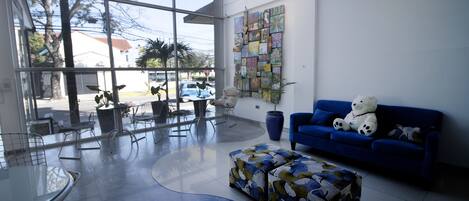 A modern lobby with a glass wall, a blue sofa, a glass table, and a patterned ottoman.