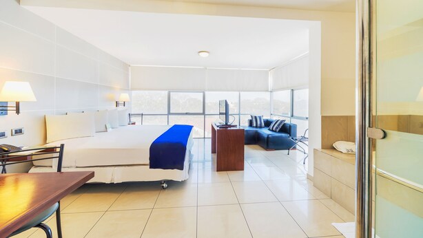 Une chambre d’hôtel moderne équipée d’un grand lit, d’un bureau, d’une chaise, d’une petite table, d’un canapé et d’une télévision.