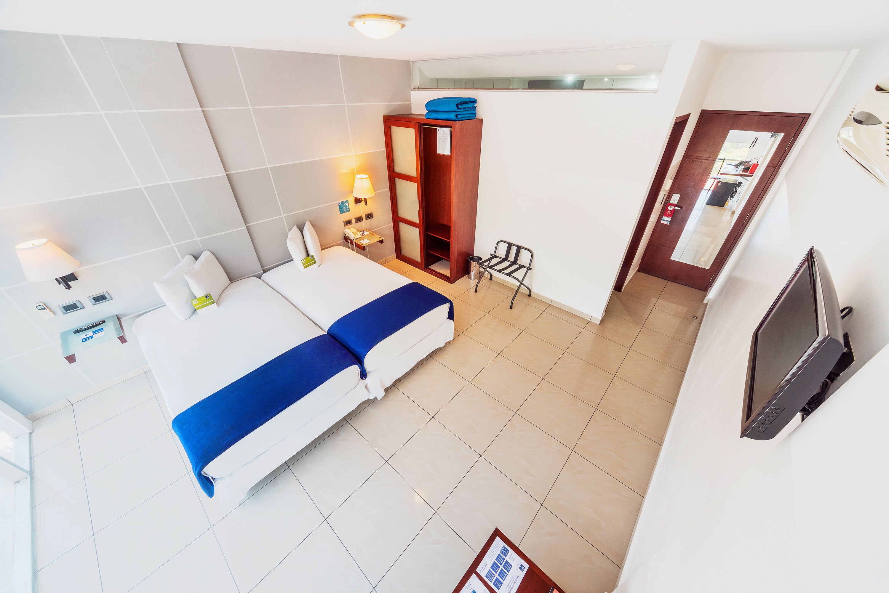 Une chambre d’hôtel comprenant un lit, une armoire, un bureau avec une lampe, une chaise et un téléviseur.