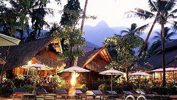 A pool area with lounge chairs and umbrellas, surrounded by tropical vegetation and thatched-roof structures. - Banpu Koh Chang (Ko Chang)