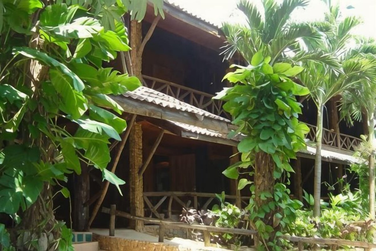 A wooden building with a balcony, surrounded by lush greenery.