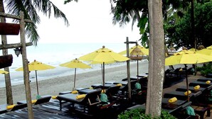 A beachside lounge area with wooden benches and yellow umbrellas, overlooking the ocean. - Banpu Koh Chang (Ko Chang)
