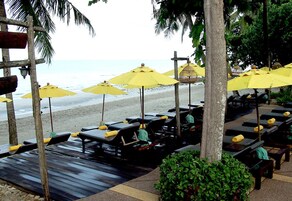 Eine Strandlounge mit Holzliegen und gelben Sonnenschirmen mit Blick auf den Ozean.