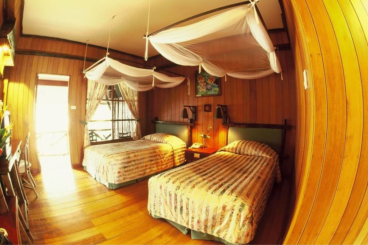 A room with two beds, wooden floors, and a window with curtains.