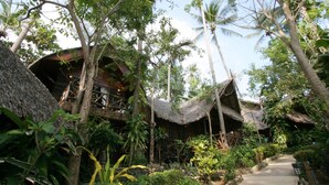 A traditional thatched-roof house surrounded by lush greenery and palm trees. - Banpu Koh Chang (Ko Chang)