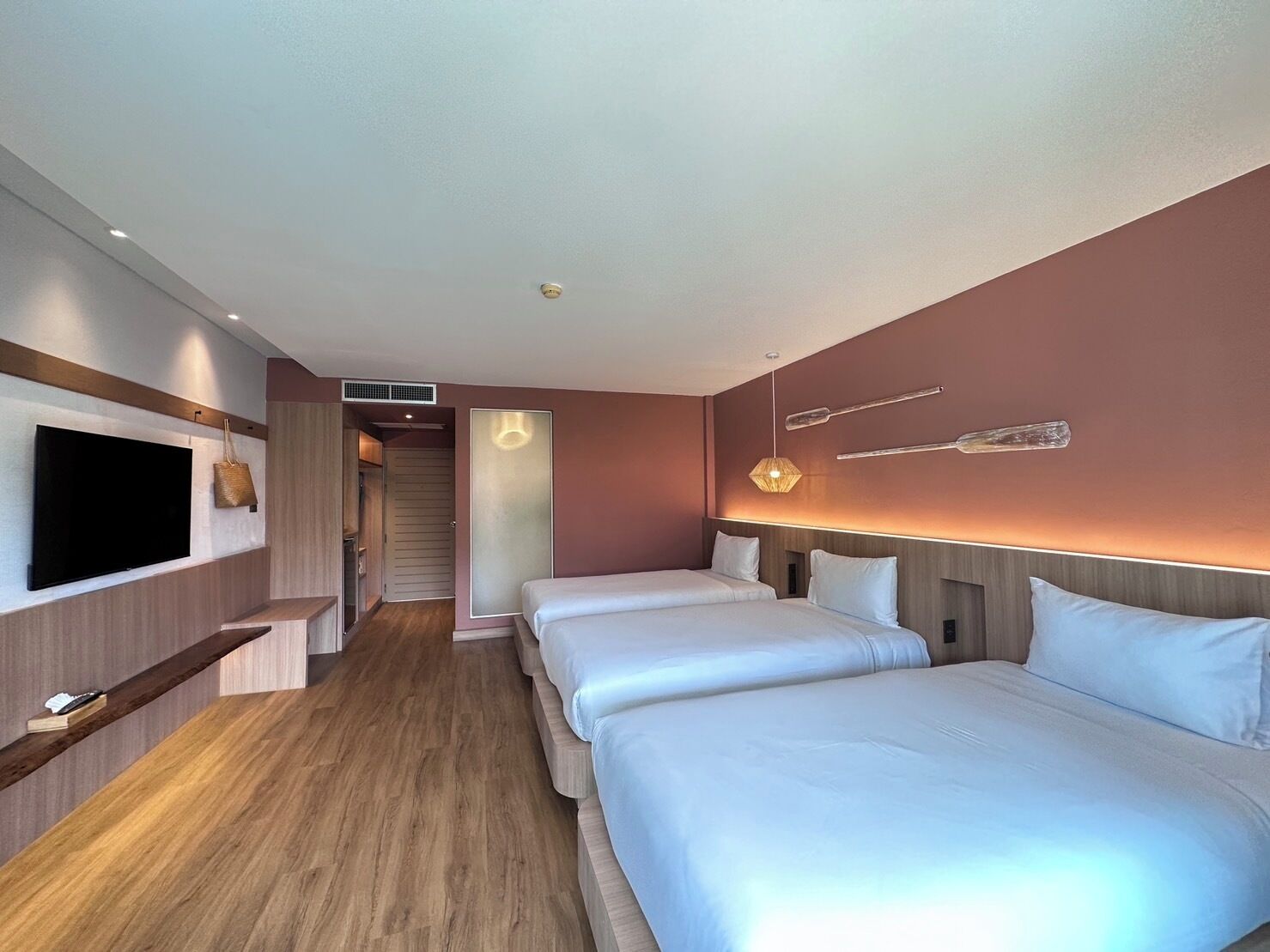 A hotel room with a TV, two beds, a wooden floor, and a hallway leading to a bathroom.