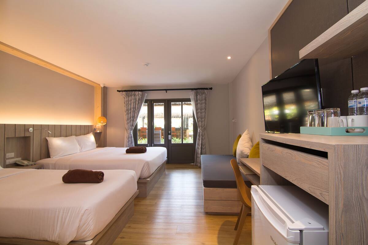 A hotel room with two beds, a desk, a television, and a view of the outdoors.