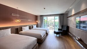 Habitación de hotel con dos camas, una zona de estar con una silla y un balcón con vistas al exterior.