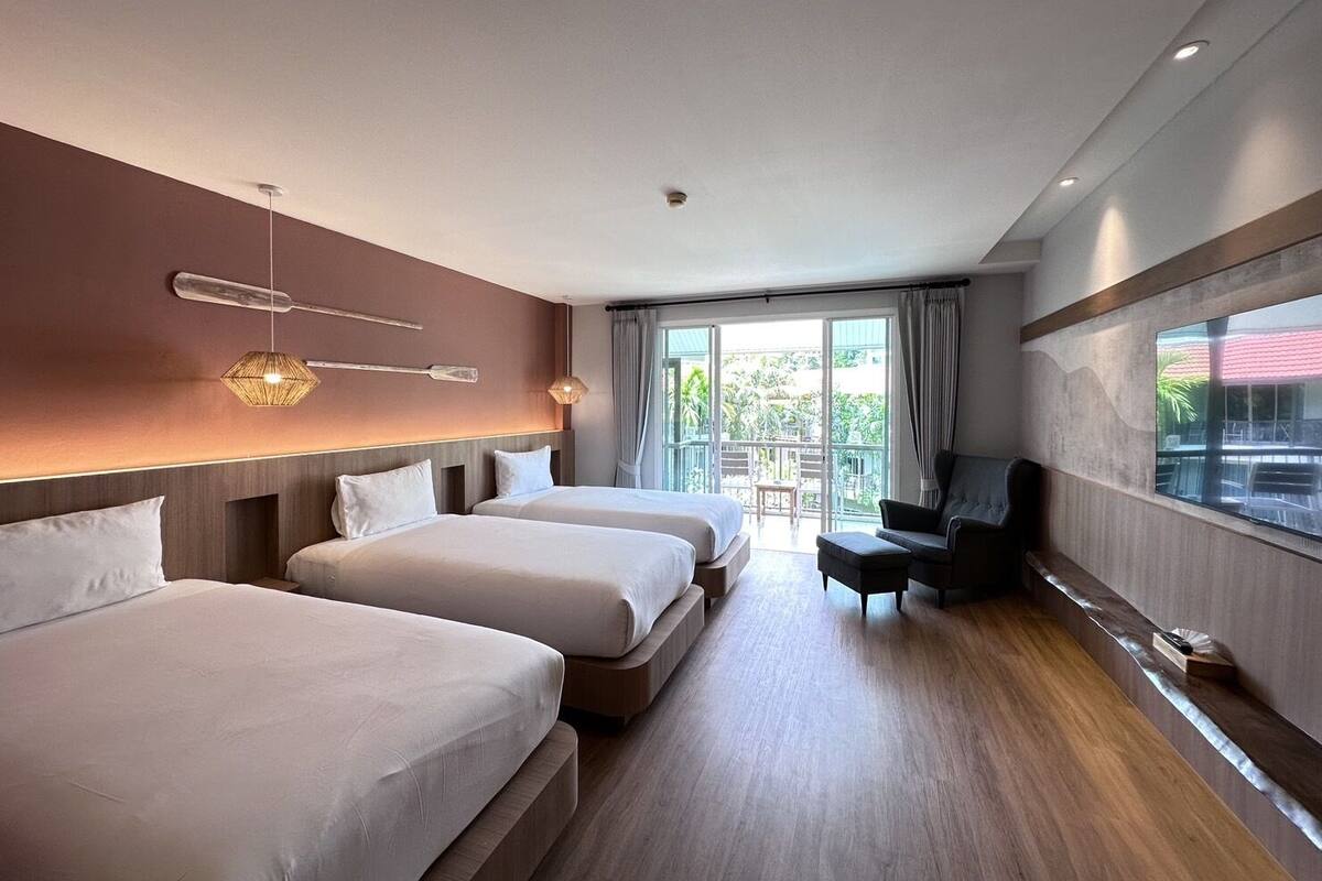 A hotel room with two beds, a seating area with a chair, and a balcony with a view of the outdoors.