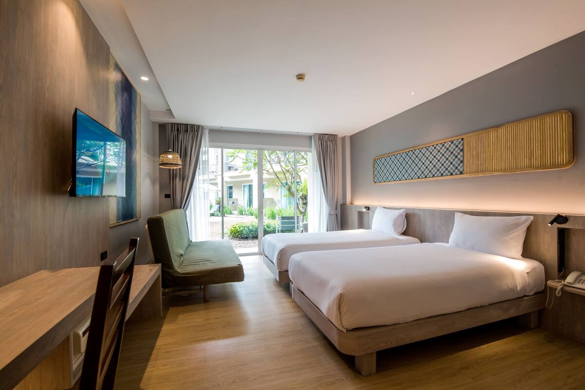 A hotel room with a bed, a desk, a chair, a TV, and a view of the outdoors.