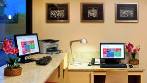Un escritorio con dos monitores, un teclado, una lámpara y un teléfono. En la pared hay cuadros enmarcados y una planta en maceta sobre el escritorio.