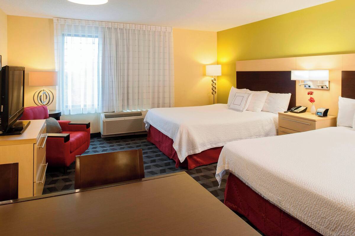Habitación de hotel con dos camas, un escritorio, una silla, un televisor y una ventana con cortinas.