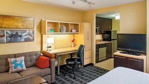 Habitación de hotel con sofá, escritorio, silla, televisor, cama, zona de cocina y baño.