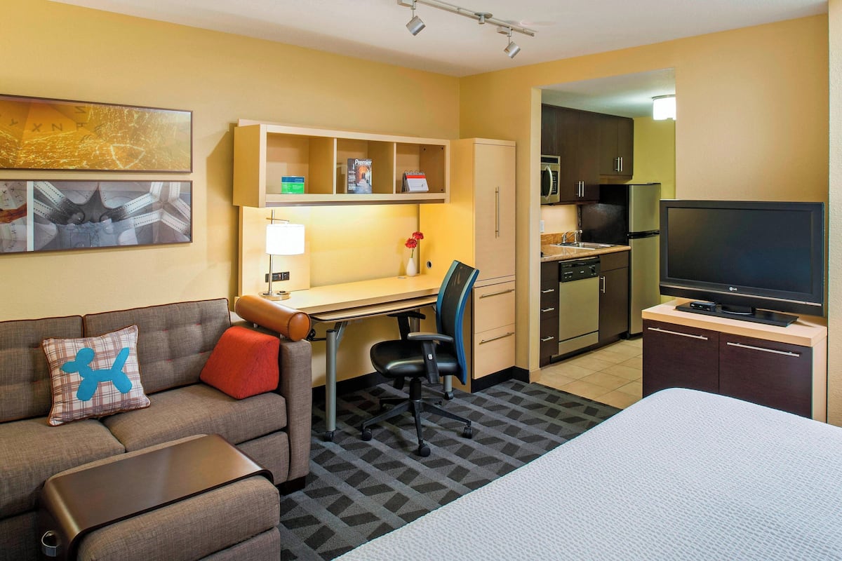 Habitación de hotel con sofá, escritorio, silla, televisor, cama, zona de cocina y baño.