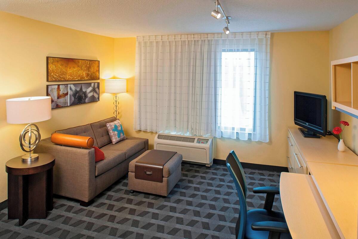 Habitación de hotel con sofá, una mesita de noche con lámpara, televisor y escritorio con silla.