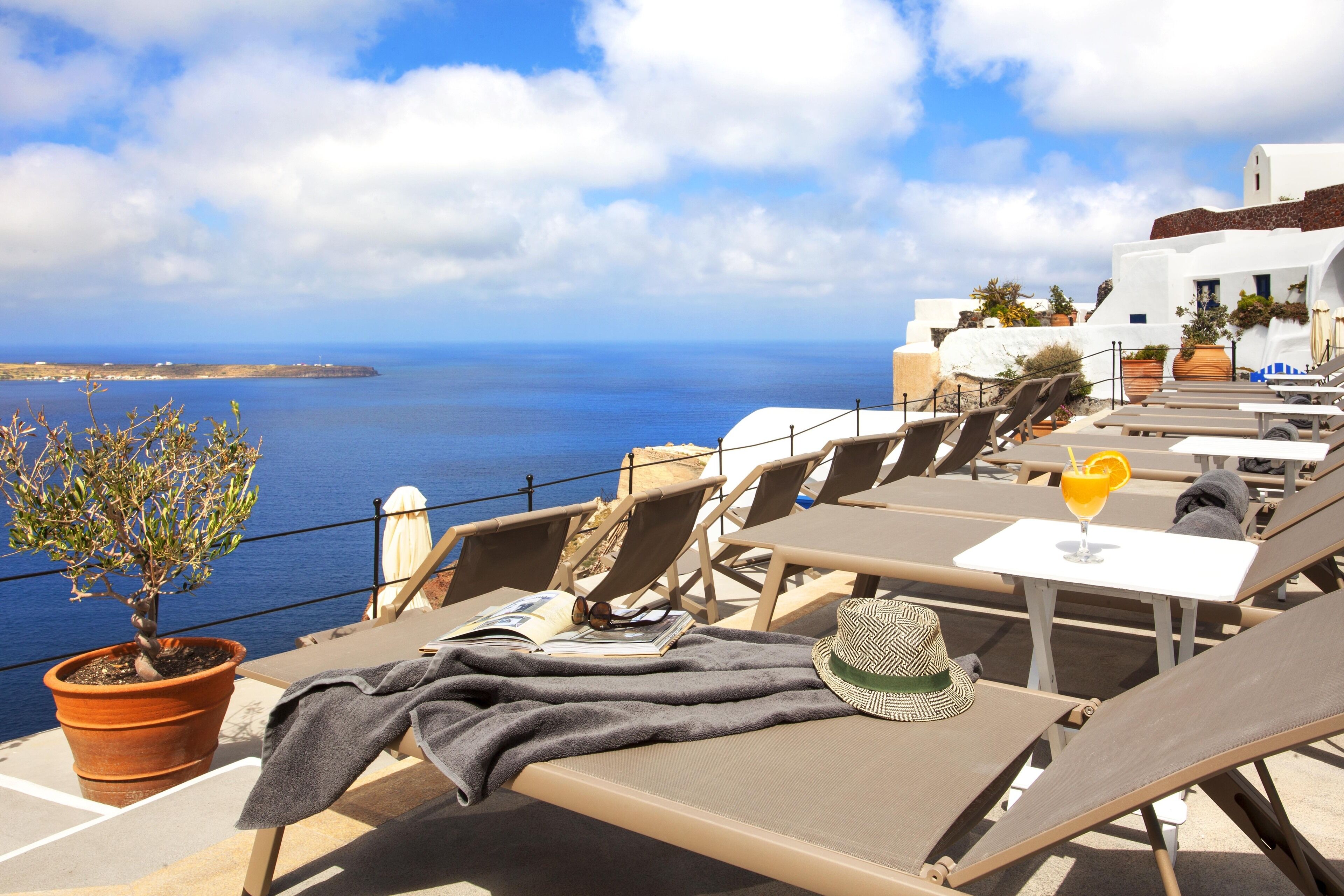 A terrace with lounge chairs, a table with a drink, and a potted plant.