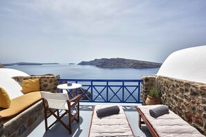 A balcony with a view of the sea, a table, and seating with cushions. - Esperas Santorini (Santorini)