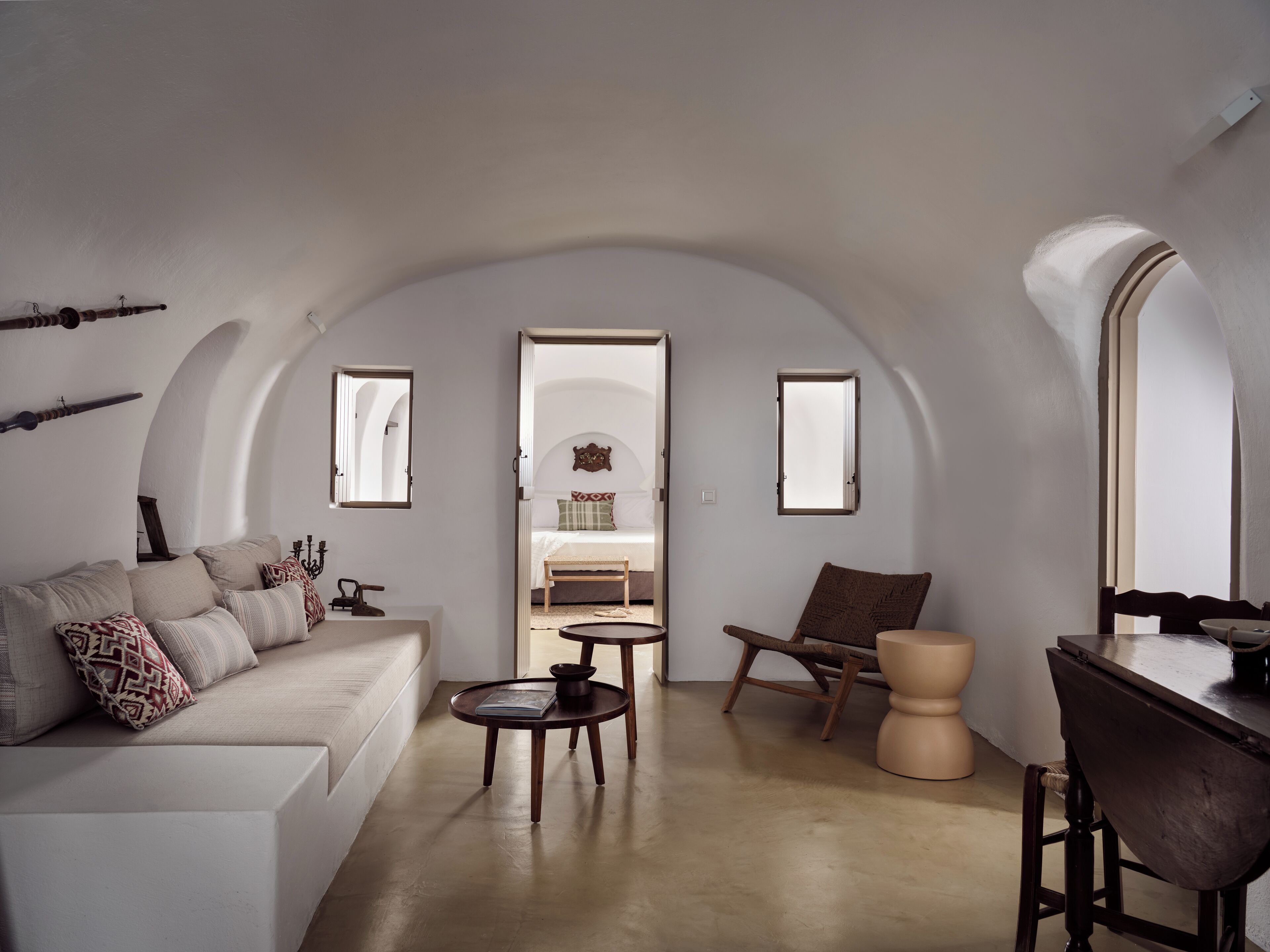 A modern, minimalist living room with a sofa, coffee table, and armchair, featuring a curved ceiling and arched windows.