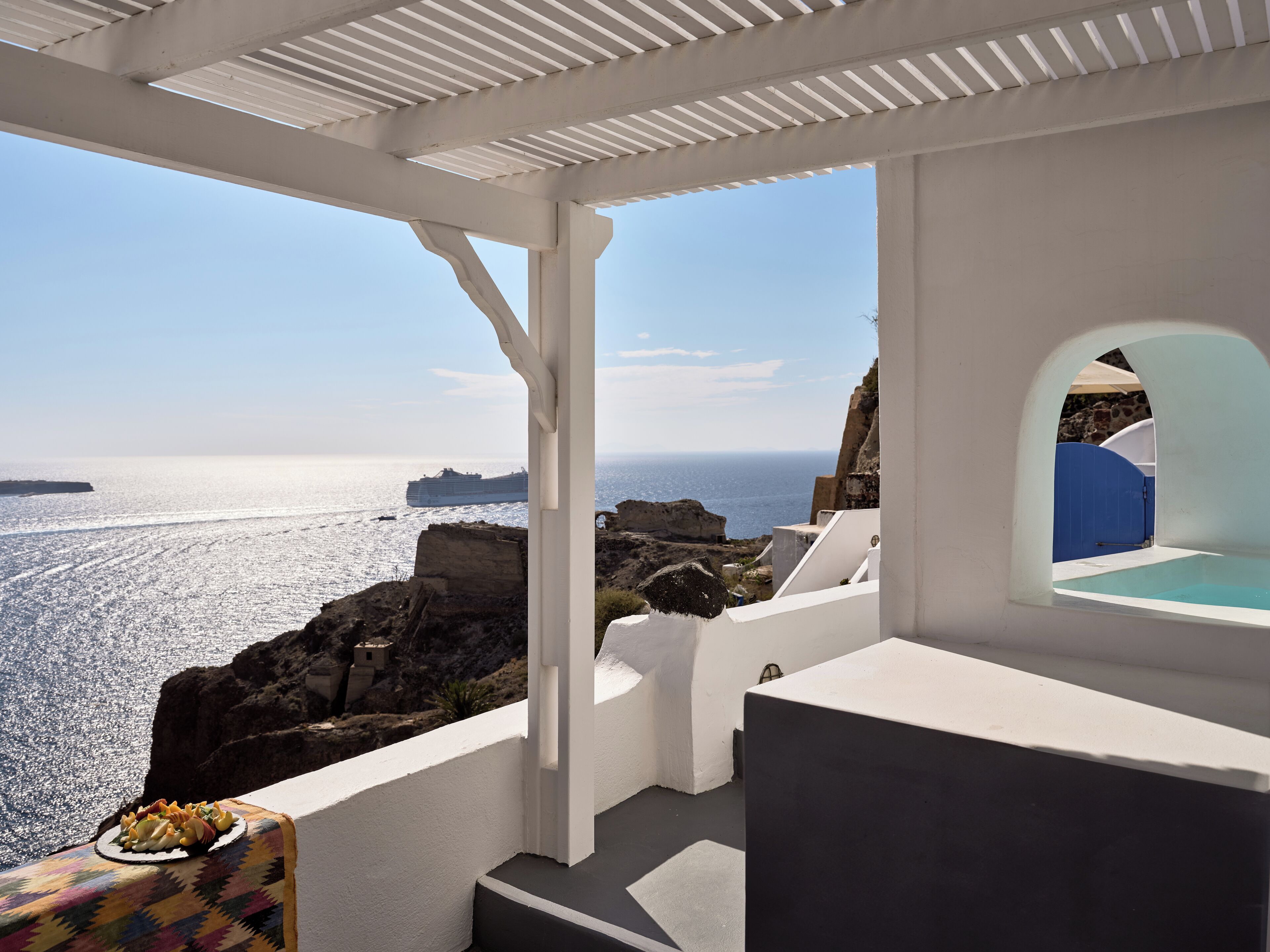 A white-walled room with a view of the sea and a cruise ship.
