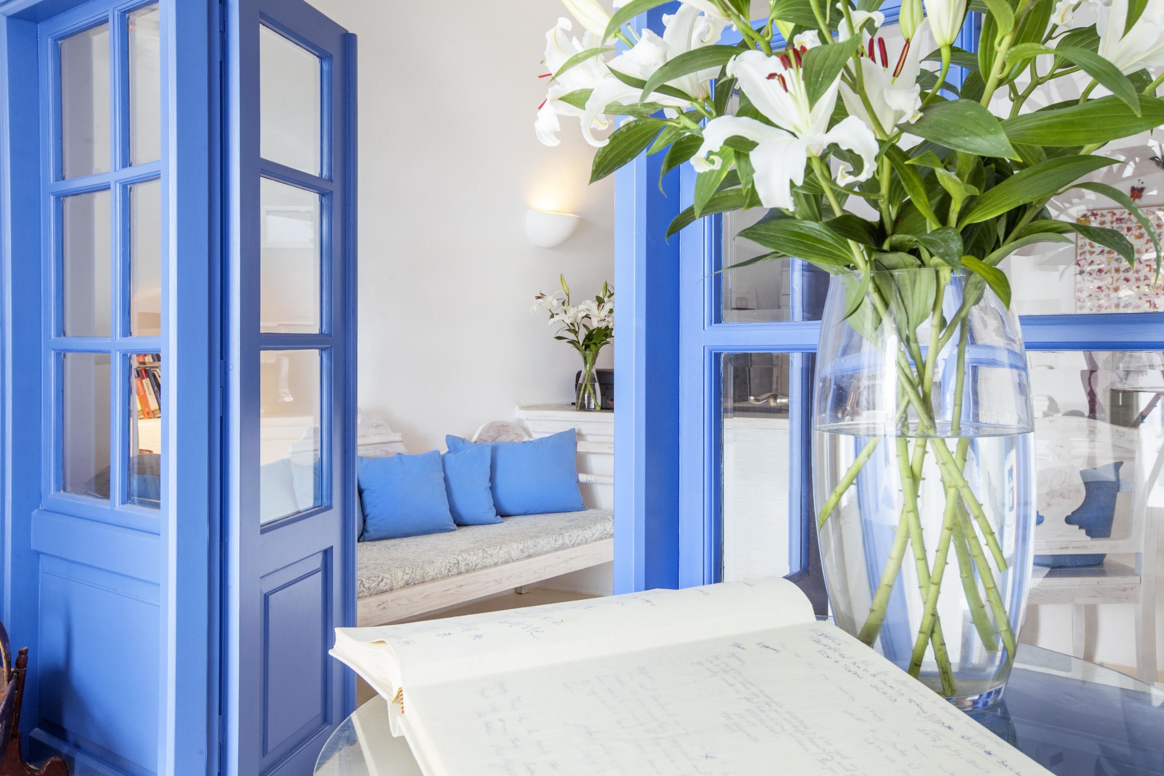 A room with a blue door, a white sofa with blue cushions, and a vase with white flowers on a table.