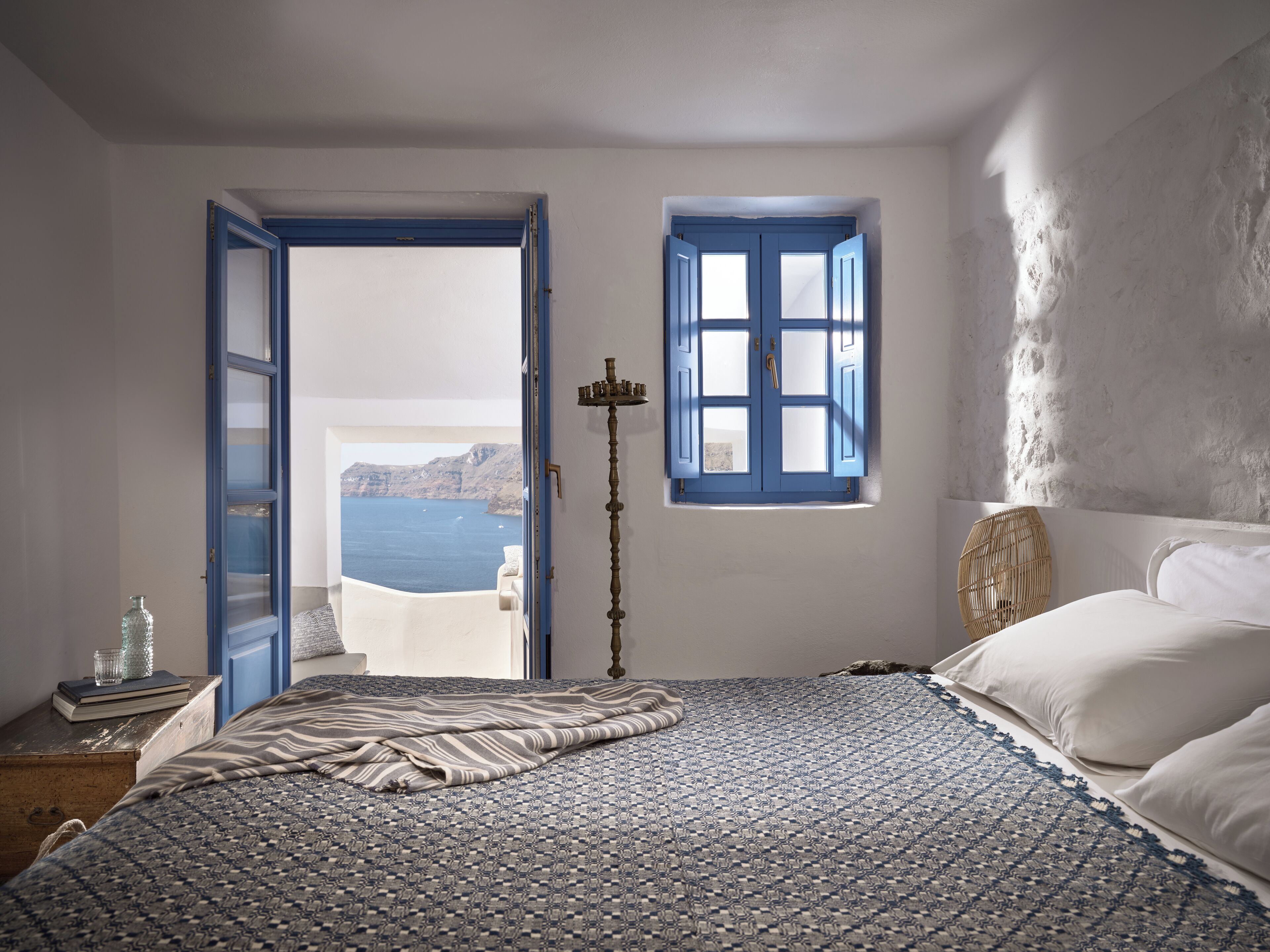 A bedroom with a bed, a window with a view of the sea, and a door leading outside.