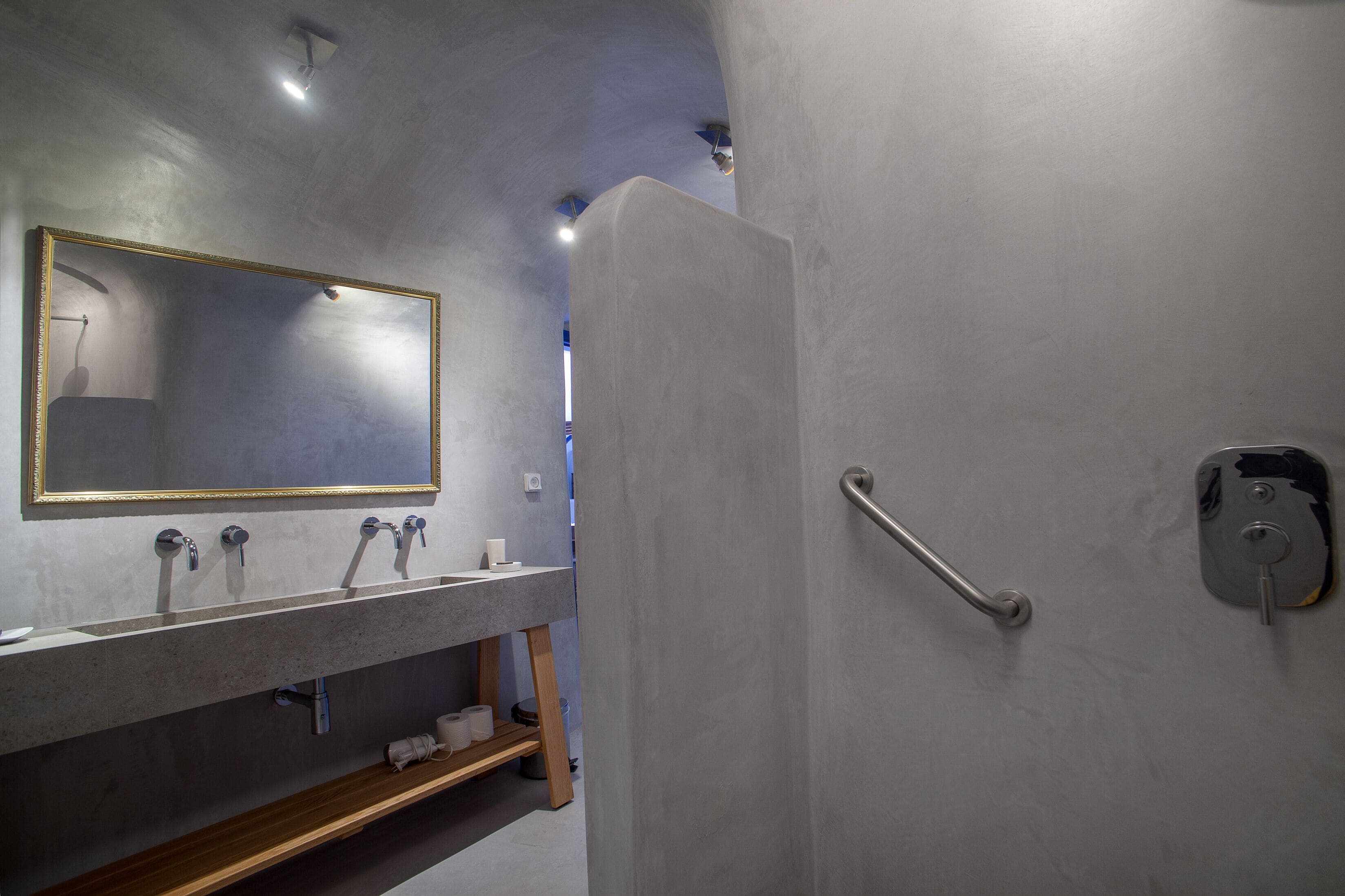 Un baño moderno con un espejo grande, tres lavamanos, una ducha y una barra de apoyo.