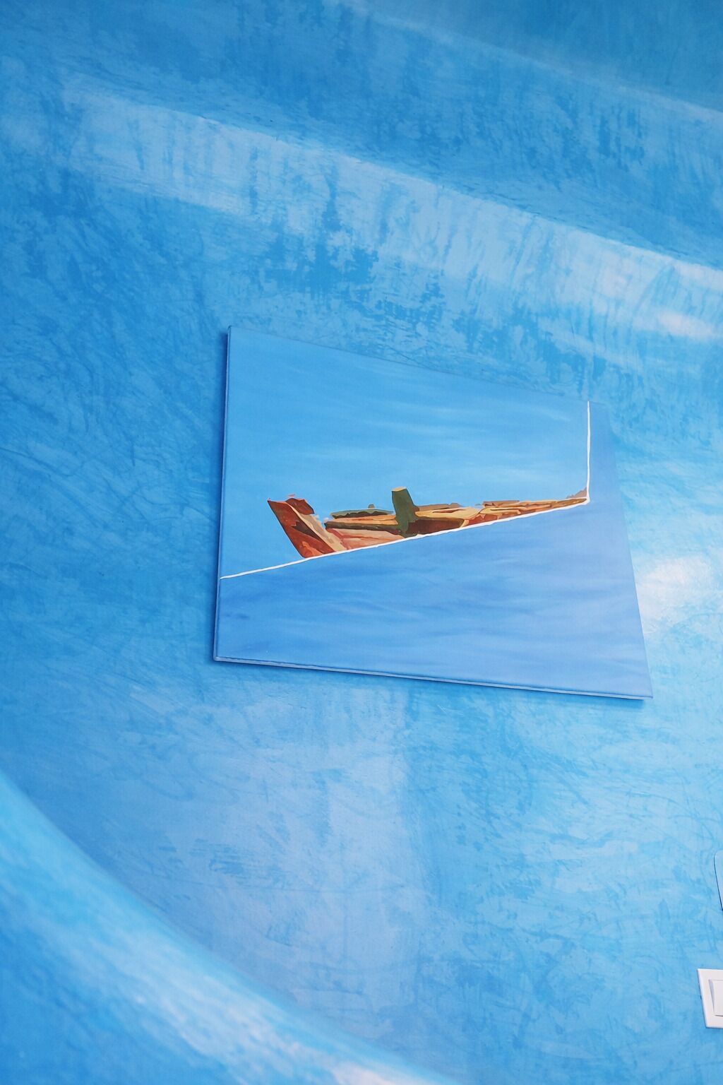 Pared azul con textura y un cuadro de un barco.