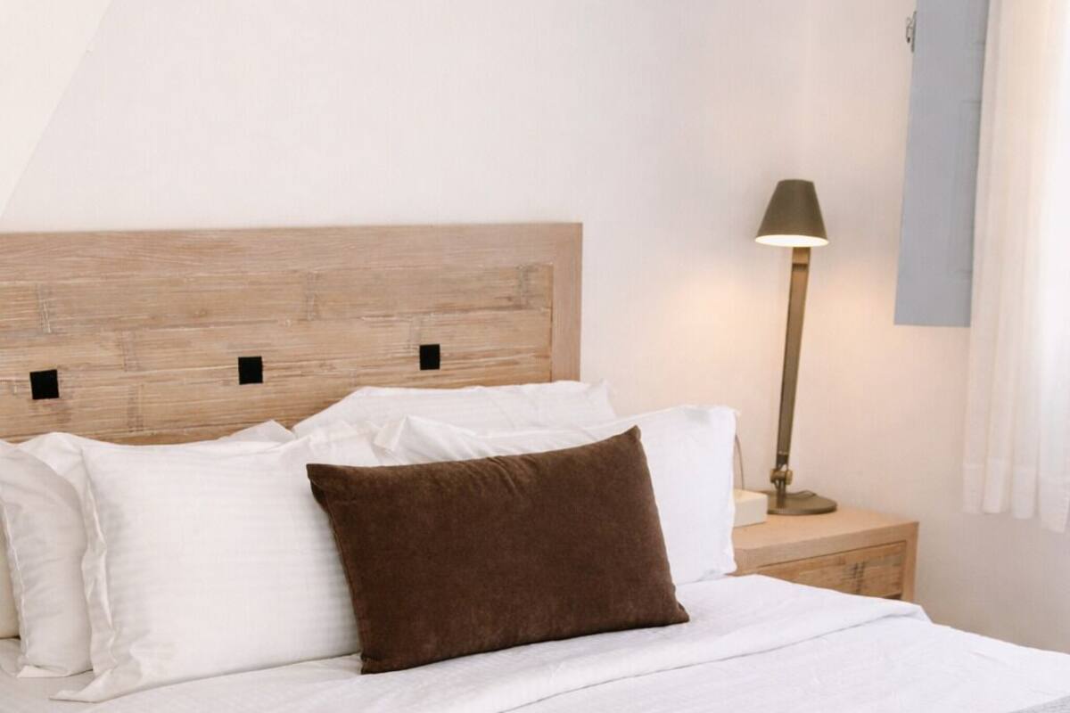 A neatly made bed with white and brown pillows, a grey throw blanket, and a wooden headboard.