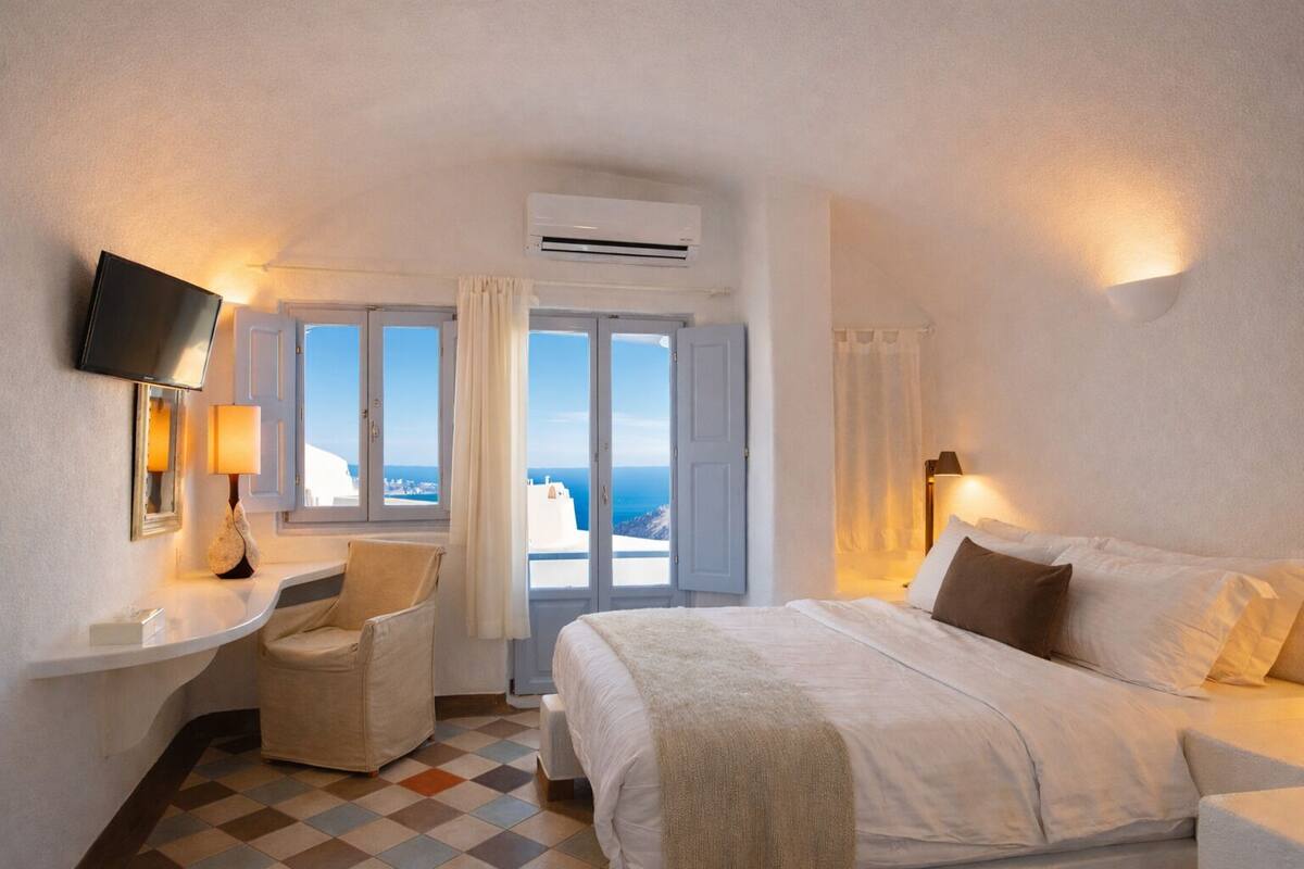 A hotel room with a bed, a desk with a lamp, a chair, and a TV.